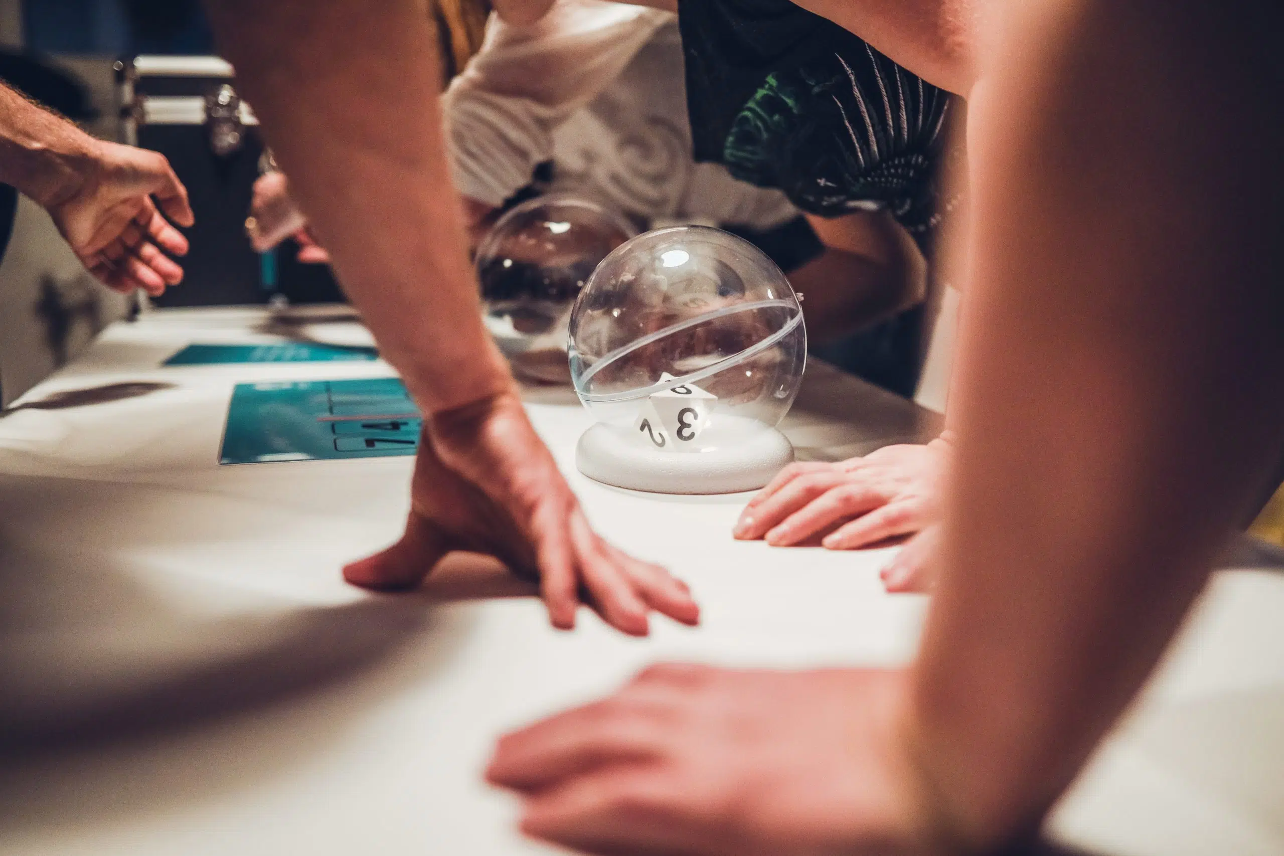 Spieltisch im FORTNOXX® Escape Room+ Hände liegen auf einem Spieltisch neben einer Plexiglaskugel mit Würfeln